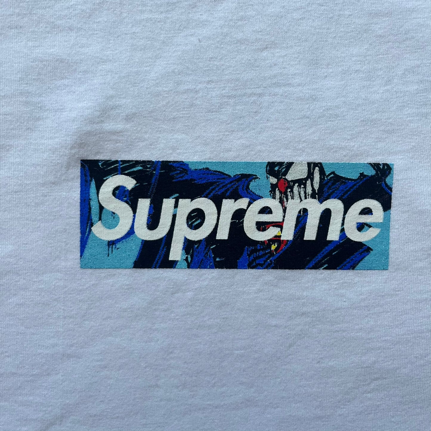 White Slawn Batpreme tee featuring a Batman-inspired graphic with iconic twist by Slawn and Supreme text overlay. Printed neck tag shows Slawn’s signature, while the back reads “This really isn’t real Supreme” in hand-drawn style with signature and logo. A striking, collectible streetwear piece.