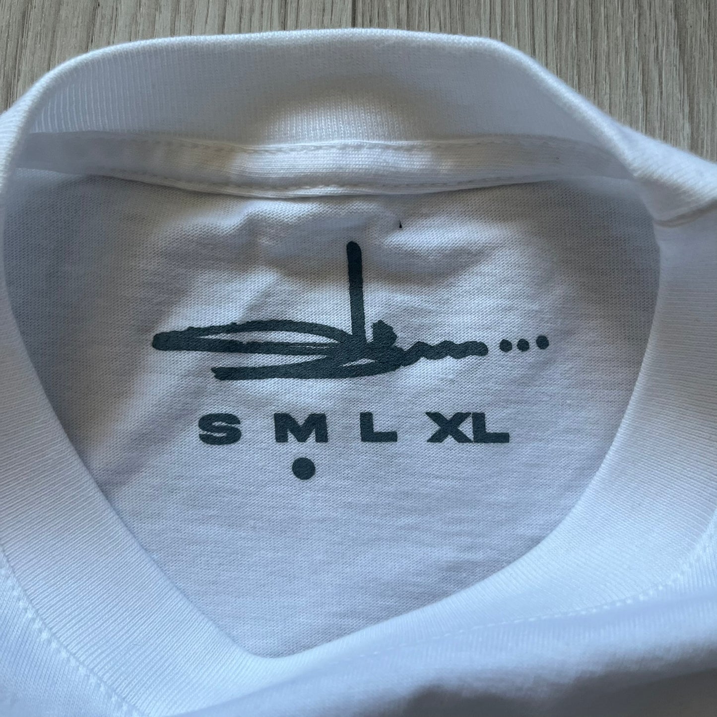 White Slawn Batpreme tee featuring a Batman-inspired graphic with iconic twist by Slawn and Supreme text overlay. Printed neck tag shows Slawn’s signature, while the back reads “This really isn’t real Supreme” in hand-drawn style with signature and logo. A striking, collectible streetwear piece.