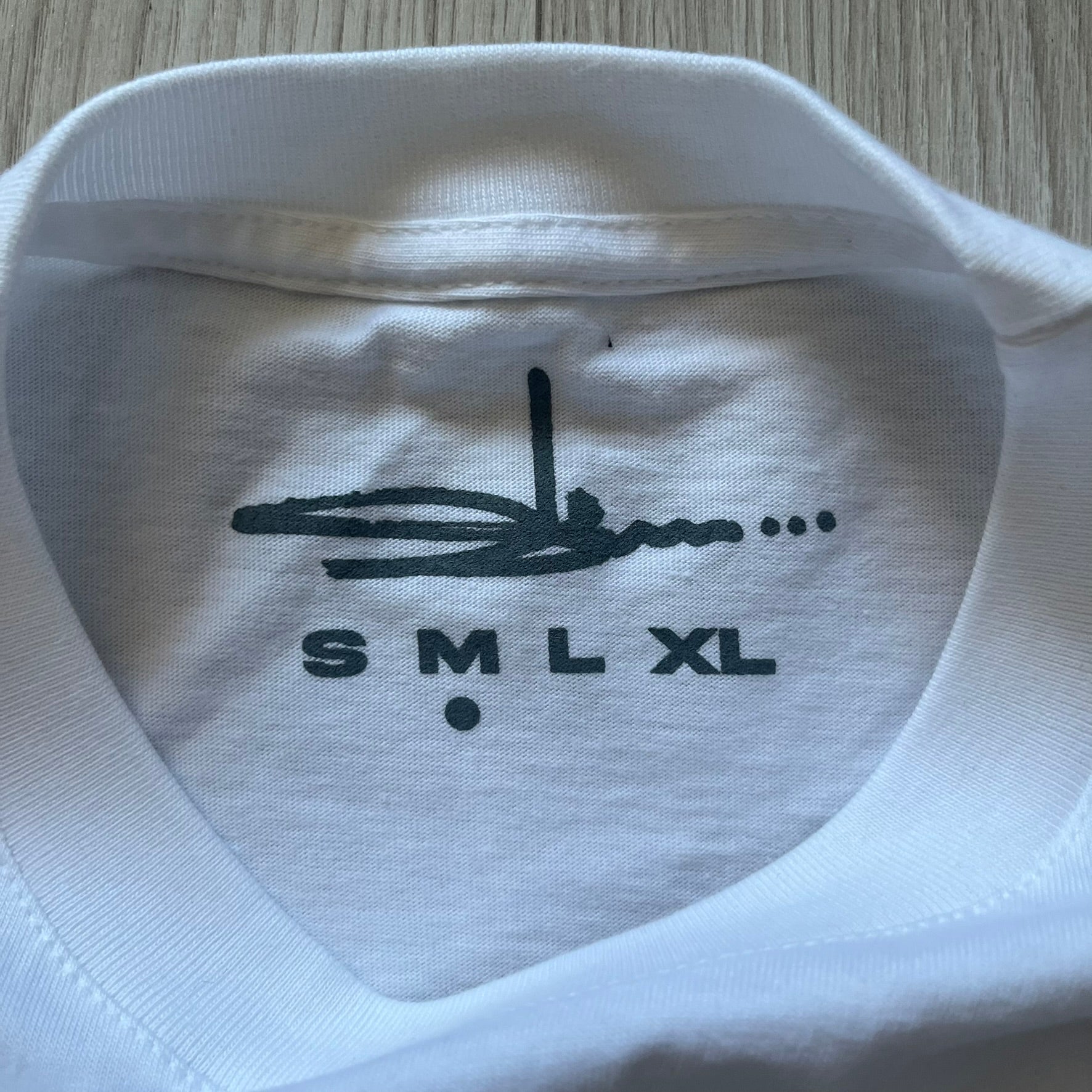 White Slawn Batpreme tee featuring a Batman-inspired graphic with iconic twist by Slawn and Supreme text overlay. Printed neck tag shows Slawn’s signature, while the back reads “This really isn’t real Supreme” in hand-drawn style with signature and logo. A striking, collectible streetwear piece.