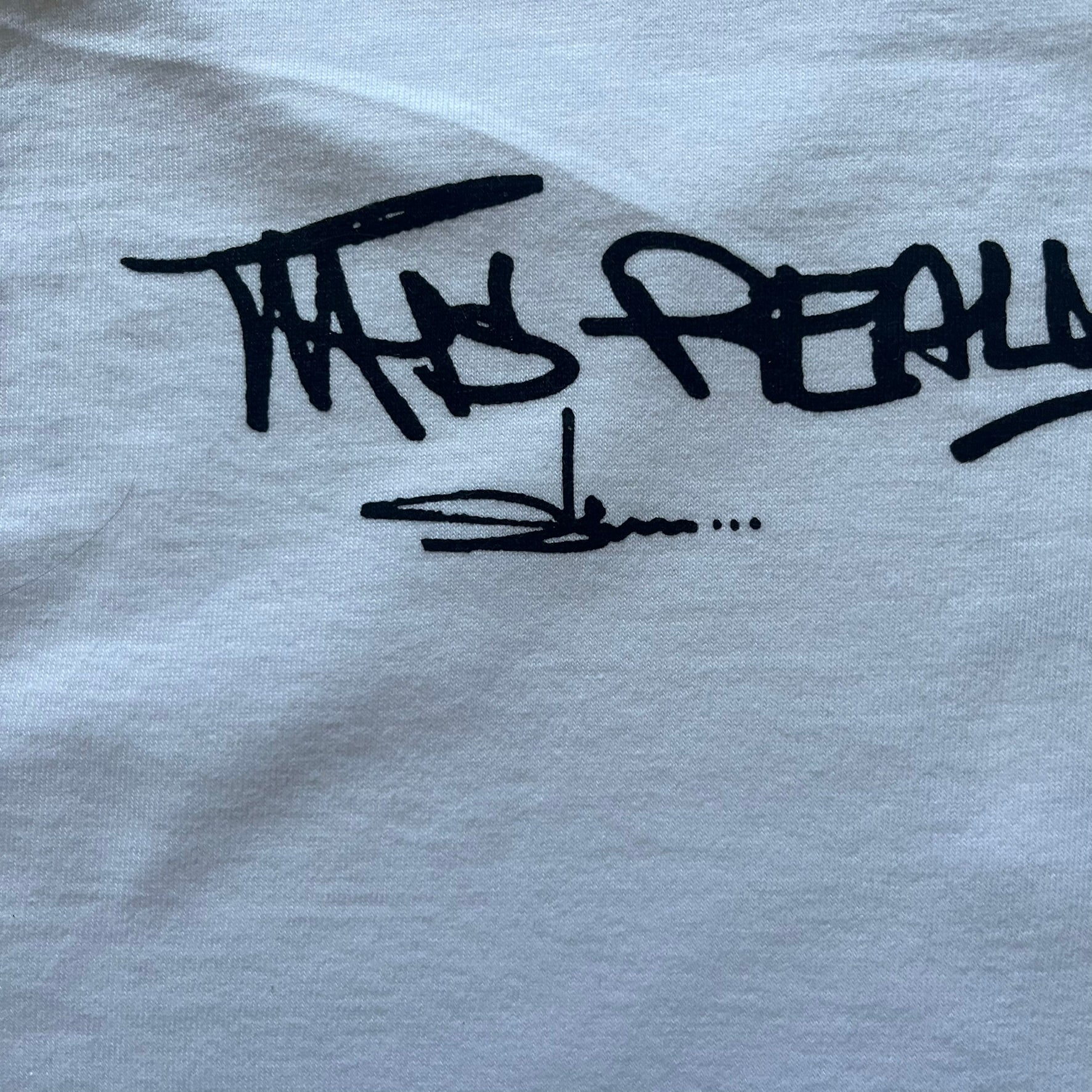 White Slawn Batpreme tee featuring a Batman-inspired graphic with iconic twist by Slawn and Supreme text overlay. Printed neck tag shows Slawn’s signature, while the back reads “This really isn’t real Supreme” in hand-drawn style with signature and logo. A striking, collectible streetwear piece.