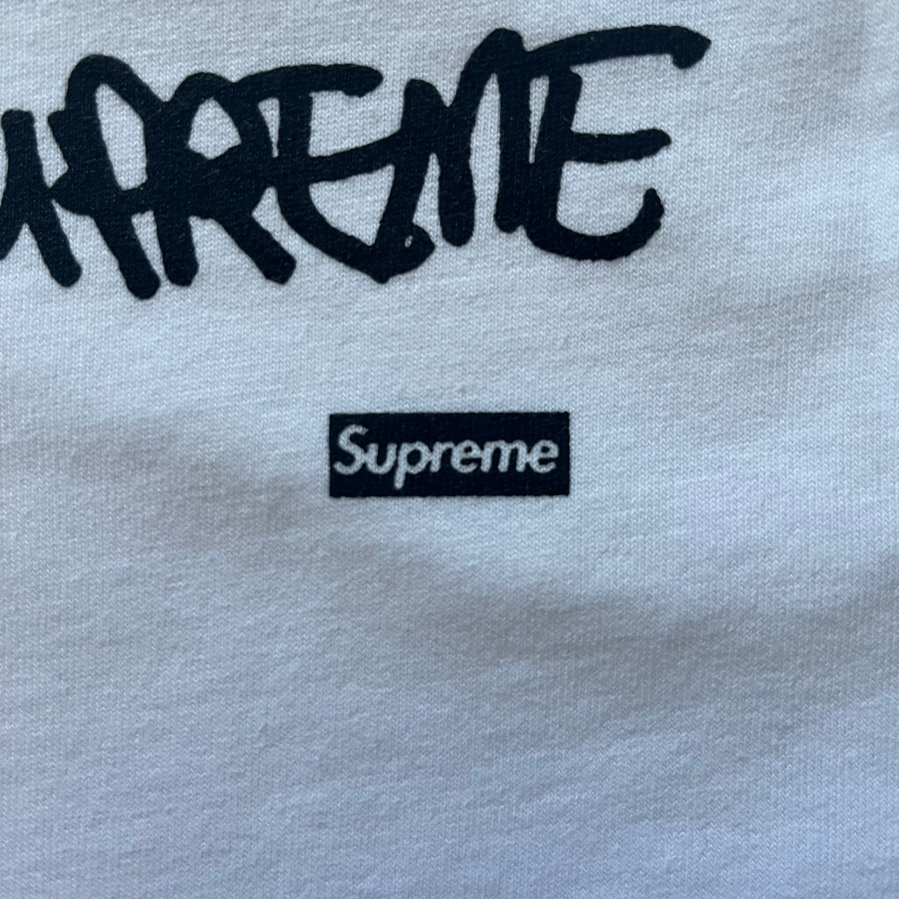 White Slawn Batpreme tee featuring a Batman-inspired graphic with iconic twist by Slawn and Supreme text overlay. Printed neck tag shows Slawn’s signature, while the back reads “This really isn’t real Supreme” in hand-drawn style with signature and logo. A striking, collectible streetwear piece.