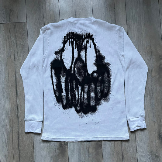 White waffle-knit / thermal long sleeve top made from textured fabric. Features a large black back print of Slawn’s dripping graffiti face, printed with fine line detail and layered ink effects. The front is finished with a small Slawn signature print near the hem, along with a neck tag bearing the artist’s signature.