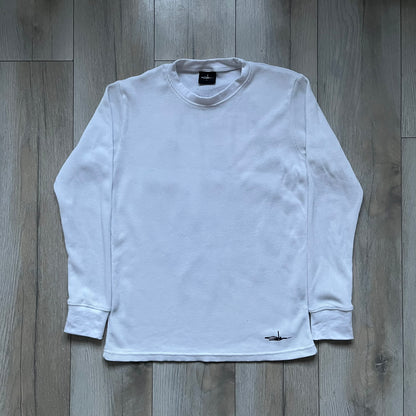 White waffle-knit / thermal long sleeve top made from textured fabric. Features a large black back print of Slawn’s dripping graffiti face, printed with fine line detail and layered ink effects. The front is finished with a small Slawn signature print near the hem, along with a neck tag bearing the artist’s signature.