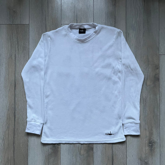 White waffle-knit / thermal long sleeve top made from textured fabric. Features a large black back print of Slawn’s dripping graffiti face, printed with fine line detail and layered ink effects. The front is finished with a small Slawn signature print near the hem, along with a neck tag bearing the artist’s signature.