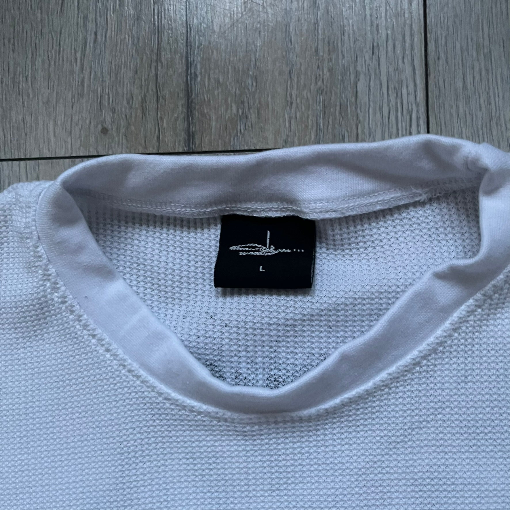 White waffle-knit / thermal long sleeve top made from textured fabric. Features a large black back print of Slawn’s dripping graffiti face, printed with fine line detail and layered ink effects. The front is finished with a small Slawn signature print near the hem, along with a neck tag bearing the artist’s signature.