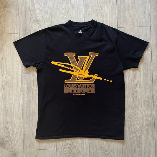 Black t-shirt with gold and brown graphic design on a wooden floor