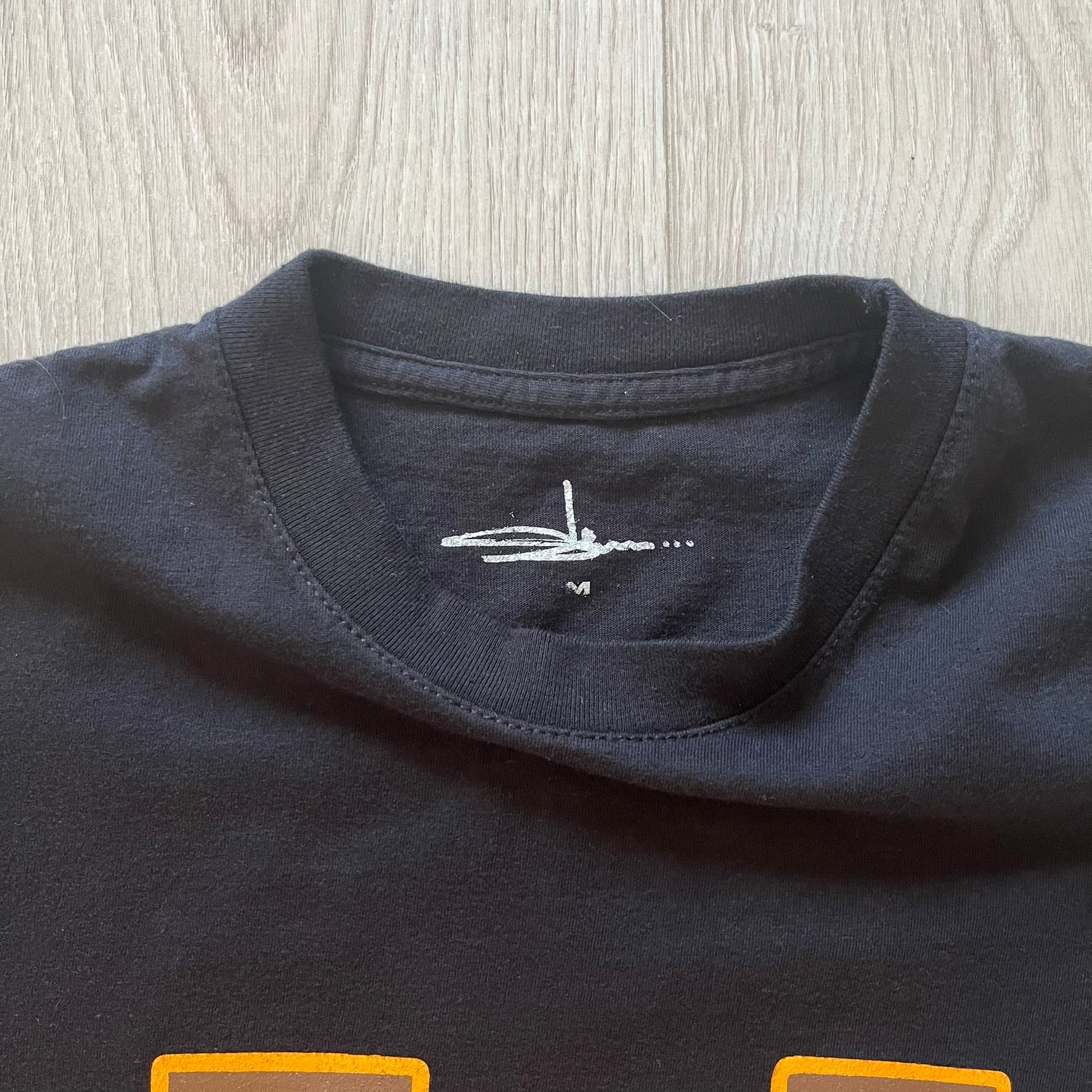 Close-up of a navy blue shirt with a small white logo on a light wooden surface