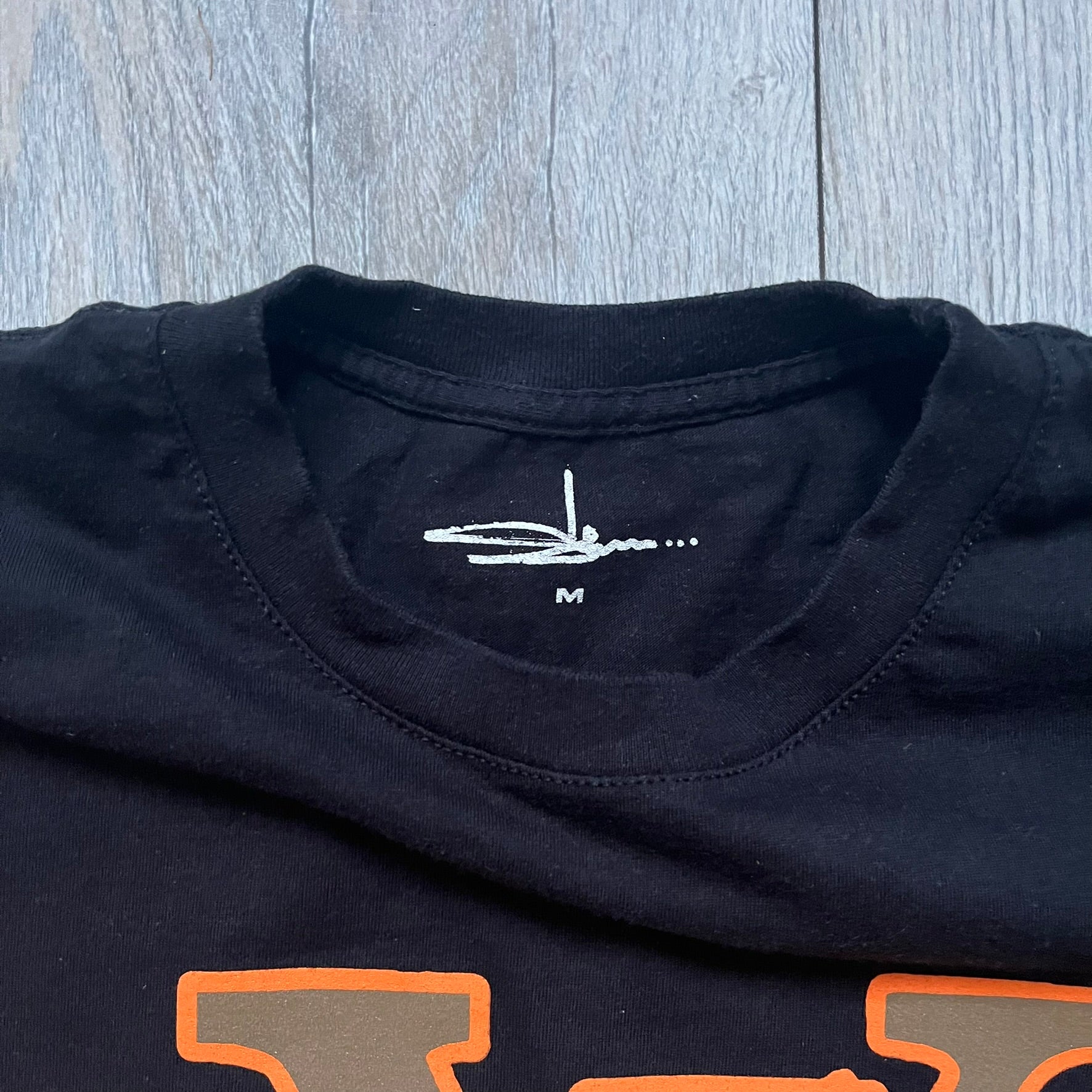 The Slawn LV Black Tee, given away at the Paris Pop-up in 2024, features a orange-brown LV logo on the front. Despite the branding, this is a Slawn creation, not an official Louis Vuitton piece.