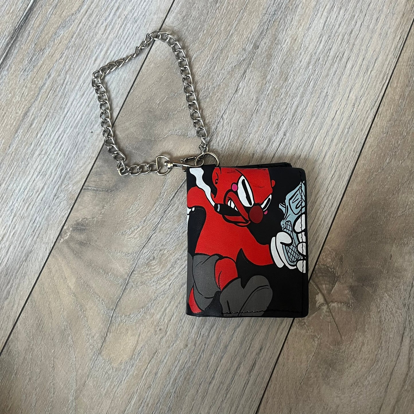 Slawn Leather Chain Man Wallet is a black foldable leather wallet featuring original artwork by Slawn on the front, depicting a red running figure holding a revolver and smoking a cigar. The wallet includes an attached metal chain for securing to clothing, along with eight card compartments and one top compartment for cash.