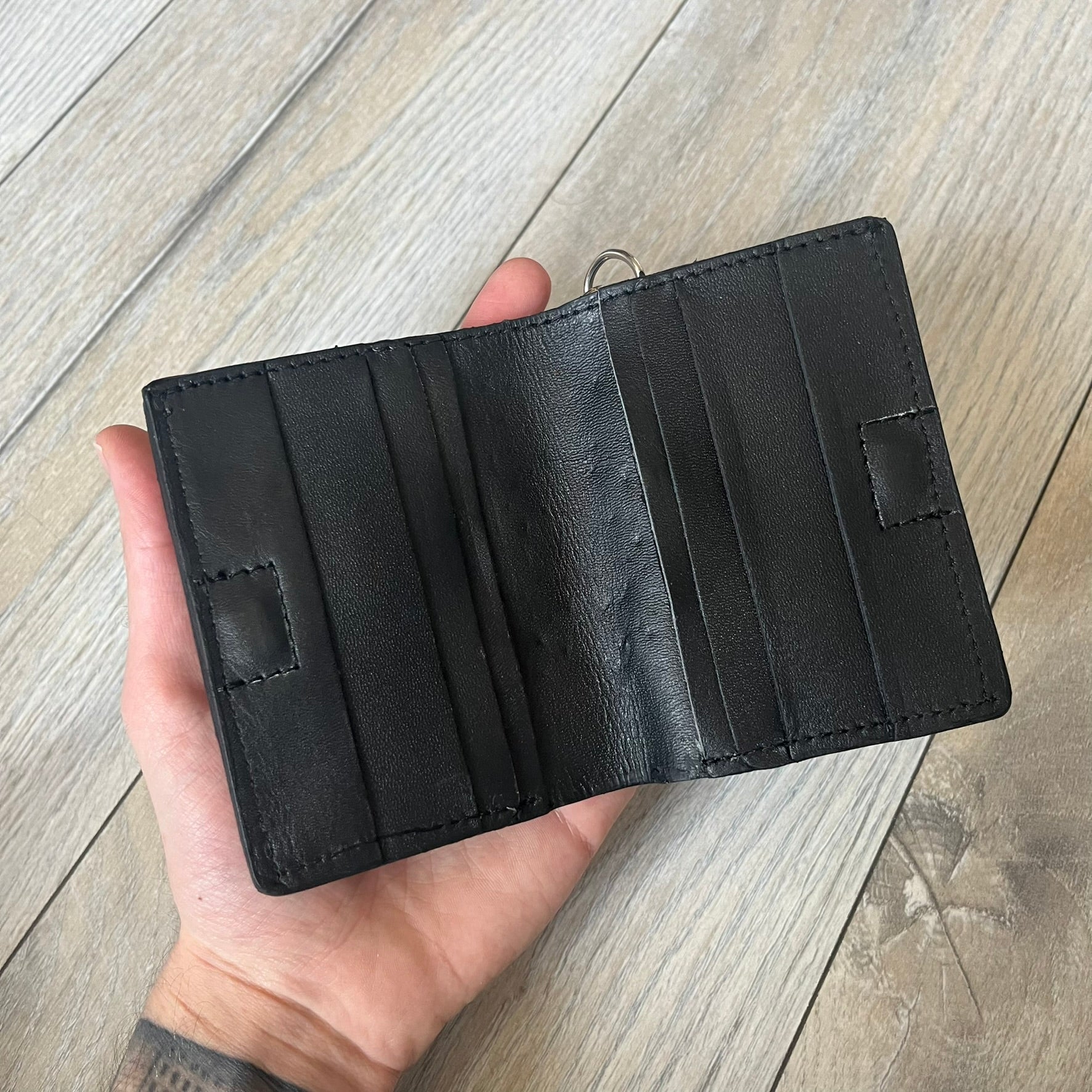 Slawn Leather Chain Man Wallet is a black foldable leather wallet featuring original artwork by Slawn on the front, depicting a red running figure holding a revolver and smoking a cigar. The wallet includes an attached metal chain for securing to clothing, along with eight card compartments and one top compartment for cash.