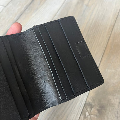 Slawn Leather Chain Man Wallet is a black foldable leather wallet featuring original artwork by Slawn on the front, depicting a red running figure holding a revolver and smoking a cigar. The wallet includes an attached metal chain for securing to clothing, along with eight card compartments and one top compartment for cash.