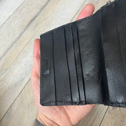Slawn Leather Chain Man Wallet is a black foldable leather wallet featuring original artwork by Slawn on the front, depicting a red running figure holding a revolver and smoking a cigar. The wallet includes an attached metal chain for securing to clothing, along with eight card compartments and one top compartment for cash.