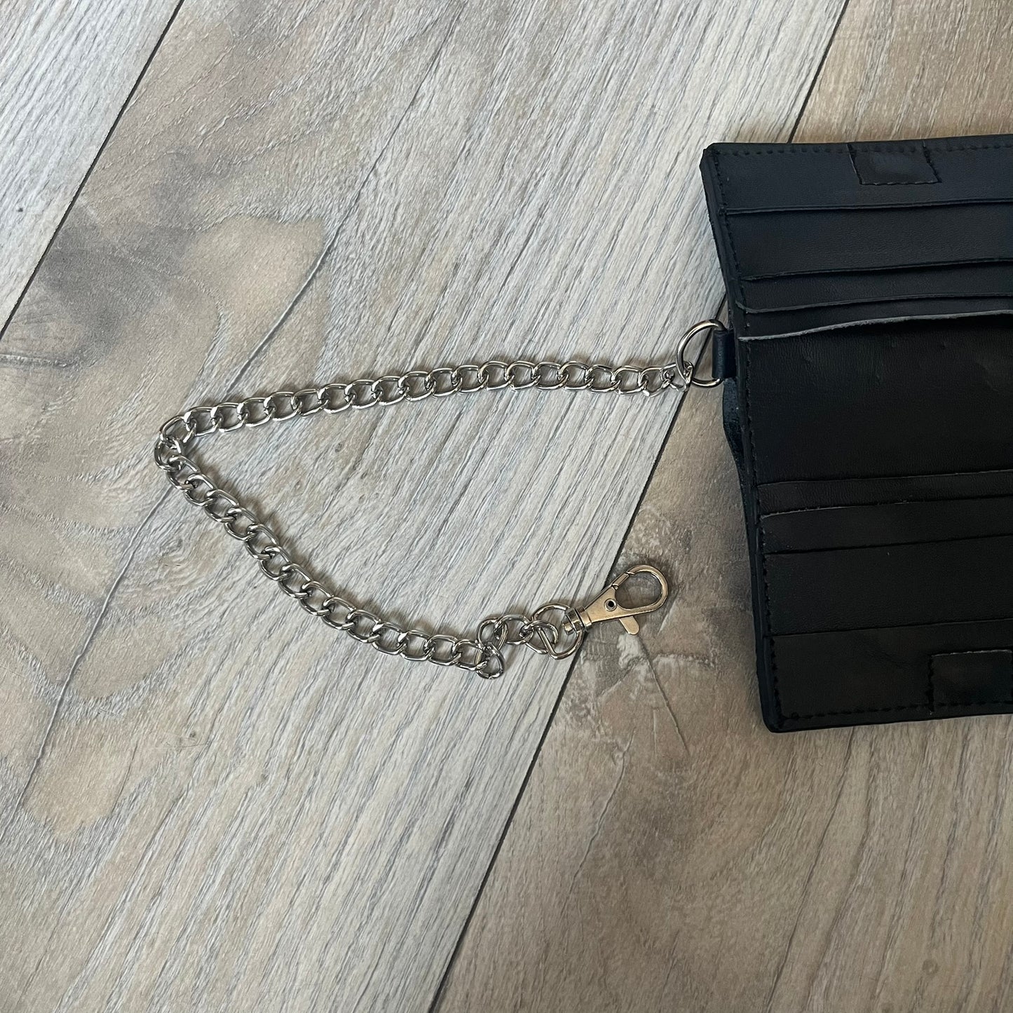 Slawn Leather Chain Man Wallet is a black foldable leather wallet featuring original artwork by Slawn on the front, depicting a red running figure holding a revolver and smoking a cigar. The wallet includes an attached metal chain for securing to clothing, along with eight card compartments and one top compartment for cash.