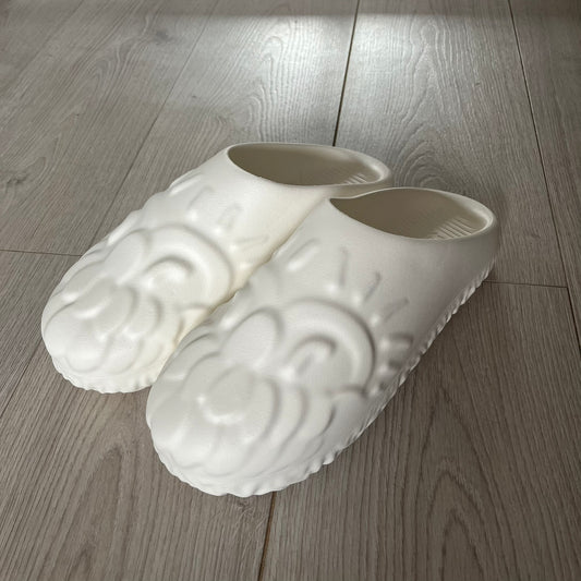 Slawn Shapes Snow Stompaz Sliders in the white colorway, created in collaboration with artist Olaolu Slawn and Shape Shoes. These closed-toe rubber sliders feature Slawn’s signature cartoonish face design forming the body of the shoe and the playful tagline “F*ck Crusty Toes.” The tread is specially designed to leave a unique footprint. They come packaged in a cardboard box filled with snow-like wool and include a special silver sticker.