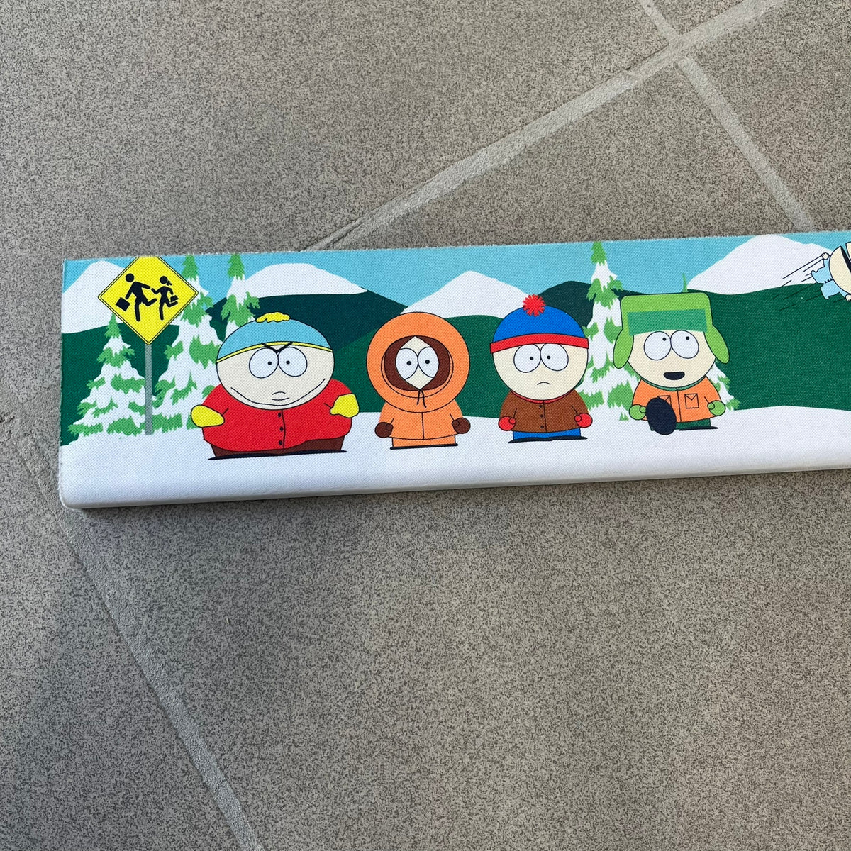 South Park 1998 Keyboard Wrist Rest is a thick foam wrist rest featuring the iconic bus stop scene with Cartman, Kenny, Stan, and Kyle kicking Ike. The design includes the wooden South Park sign and a small 1998 Comedy Central licensing mark, with a black base.