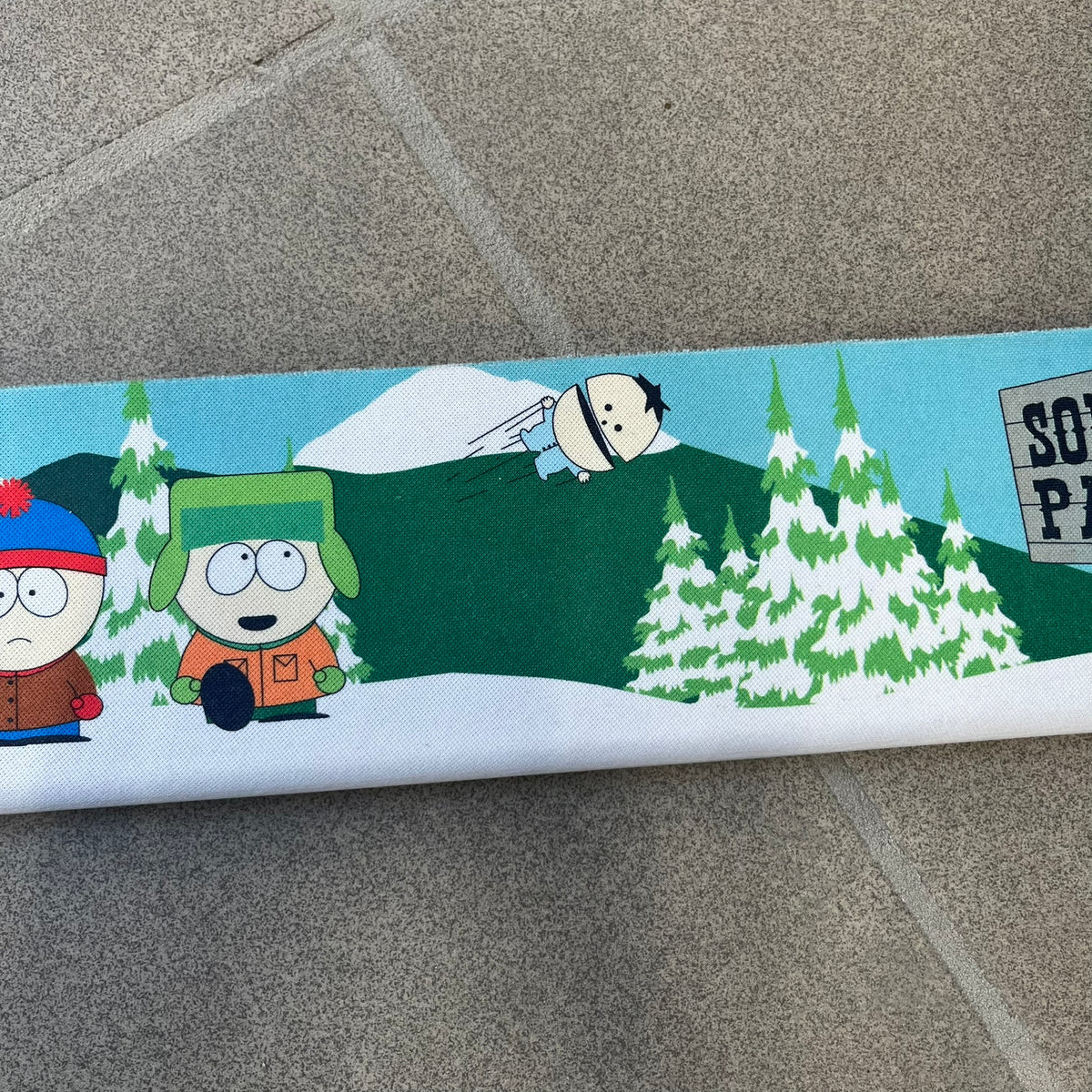 South Park 1998 Keyboard Wrist Rest is a thick foam wrist rest featuring the iconic bus stop scene with Cartman, Kenny, Stan, and Kyle kicking Ike. The design includes the wooden South Park sign and a small 1998 Comedy Central licensing mark, with a black base.