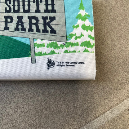 South Park 1998 Keyboard Wrist Rest is a thick foam wrist rest featuring the iconic bus stop scene with Cartman, Kenny, Stan, and Kyle kicking Ike. The design includes the wooden South Park sign and a small 1998 Comedy Central licensing mark, with a black base.