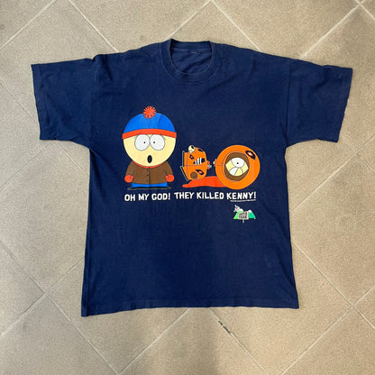 South Park 1998 “They Killed Kenny” Navy Tee features a a front graphic of Stan standing with a surprised expression next to a fallen Kenny. Below the characters is white “Oh My God! They Killed Kenny!” text, with a small South Park logo and 1998 licensing detail printed underneath on the right side. Made from cotton.