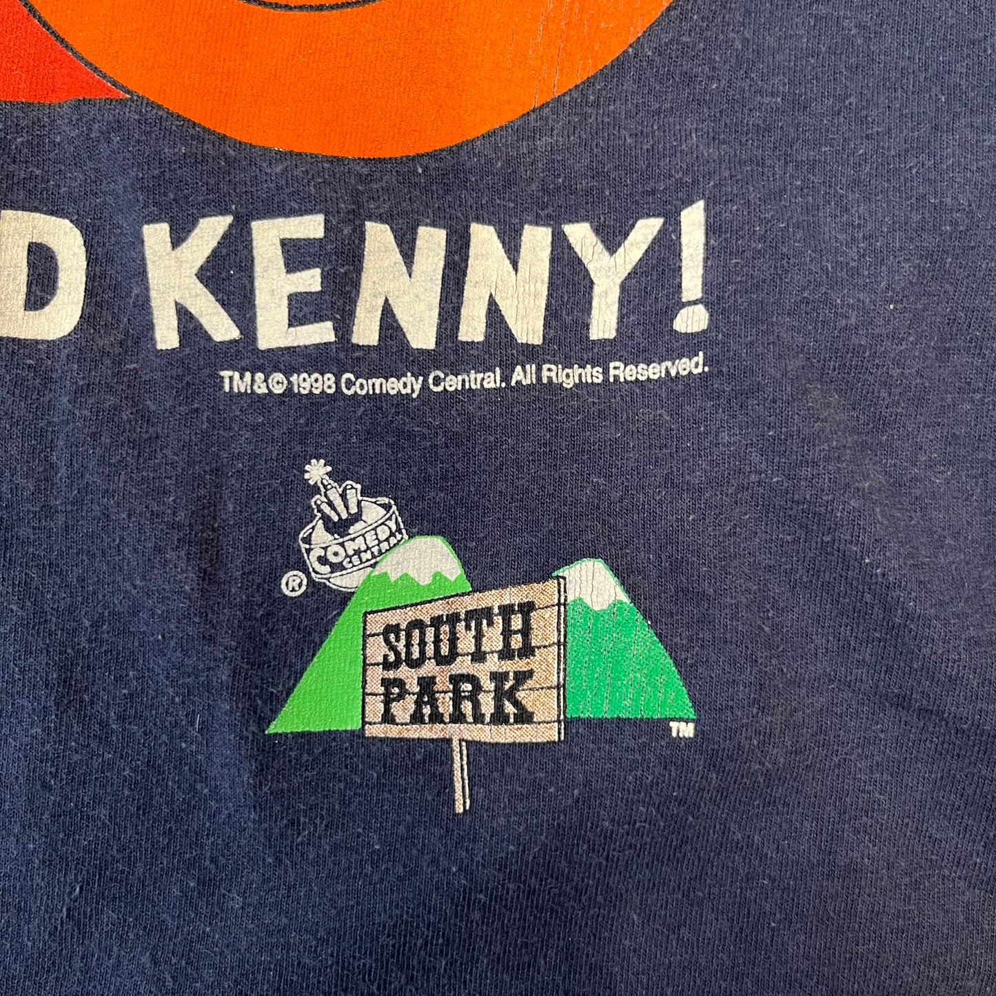 South Park 1998 “They Killed Kenny” Navy Tee features a a front graphic of Stan standing with a surprised expression next to a fallen Kenny. Below the characters is white “Oh My God! They Killed Kenny!” text, with a small South Park logo and 1998 licensing detail printed underneath on the right side. Made from cotton.