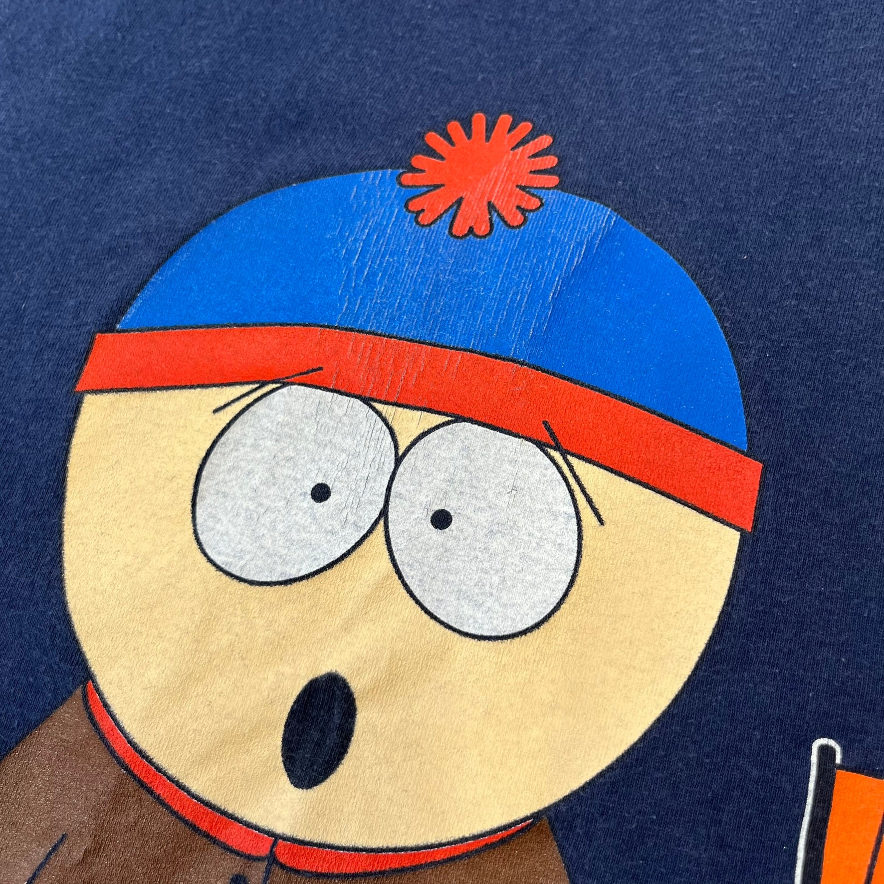 South Park 1998 “They Killed Kenny” Navy Tee features a a front graphic of Stan standing with a surprised expression next to a fallen Kenny. Below the characters is white “Oh My God! They Killed Kenny!” text, with a small South Park logo and 1998 licensing detail printed underneath on the right side. Made from cotton.