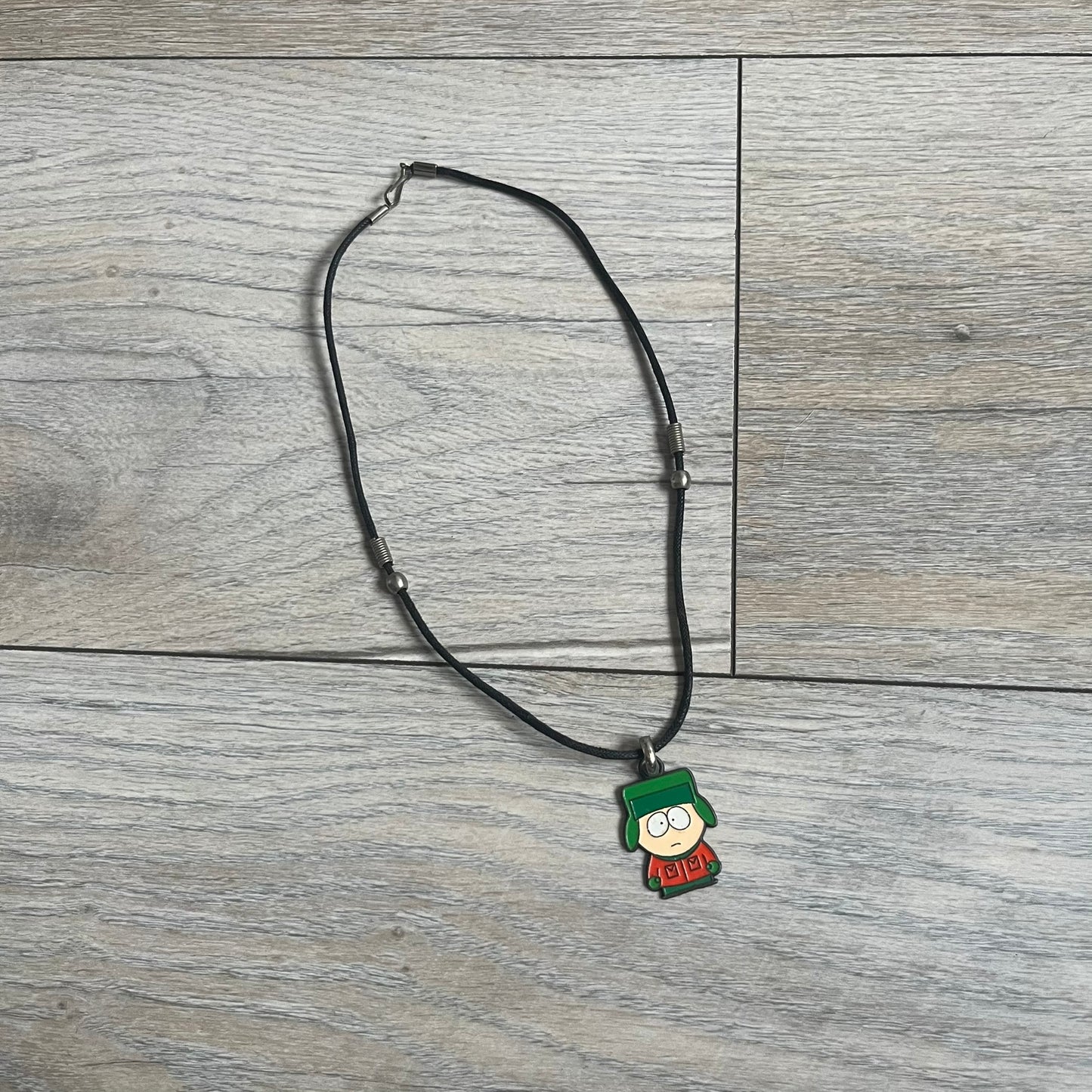 South Park 2000 Kyle Necklace features a black cord necklace with a metal pendant shaped as Kyle from South Park. The back of the pendant is marked with 2000 Comedy Central and Sedesma licensing details.