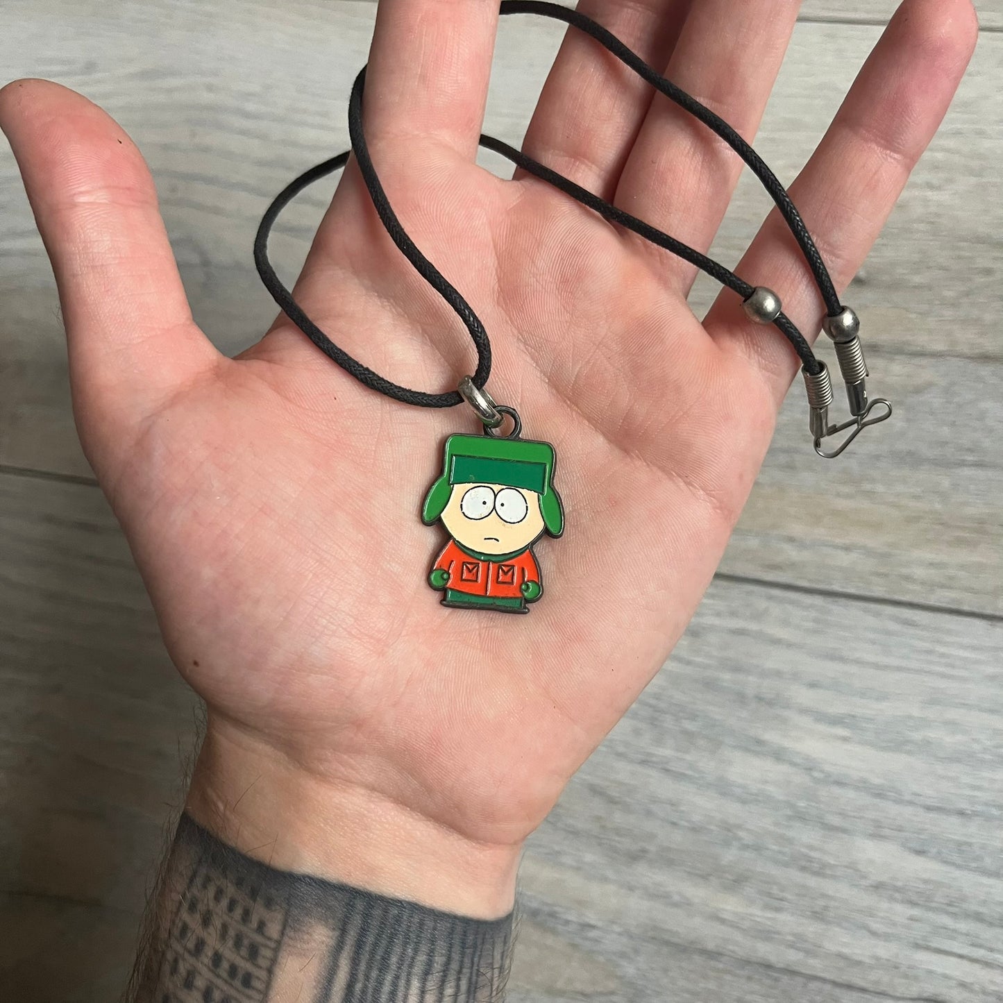 South Park 2000 Kyle Necklace features a black cord necklace with a metal pendant shaped as Kyle from South Park. The back of the pendant is marked with 2000 Comedy Central and Sedesma licensing details.