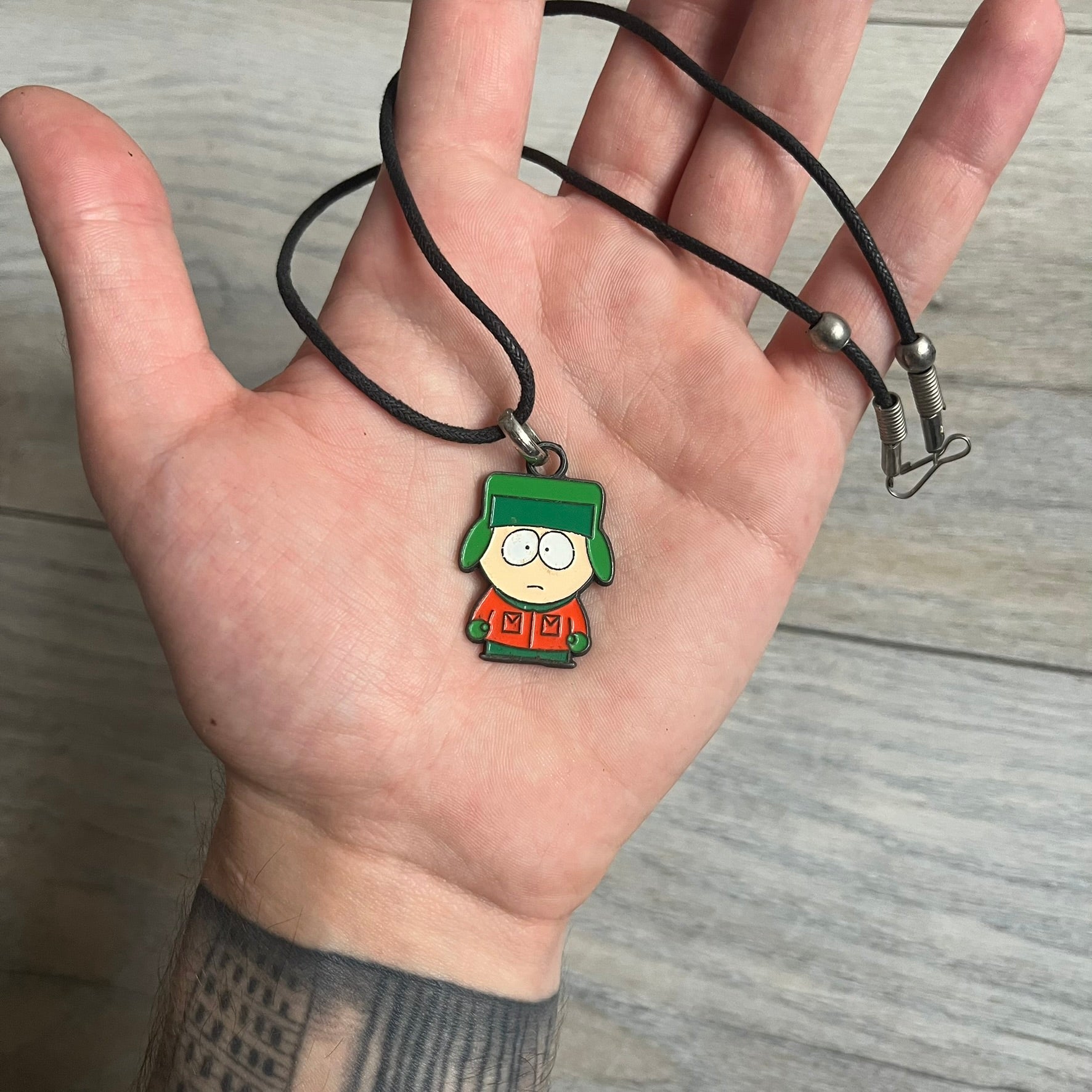 South Park 2000 Kyle Necklace features a black cord necklace with a metal pendant shaped as Kyle from South Park. The back of the pendant is marked with 2000 Comedy Central and Sedesma licensing details.