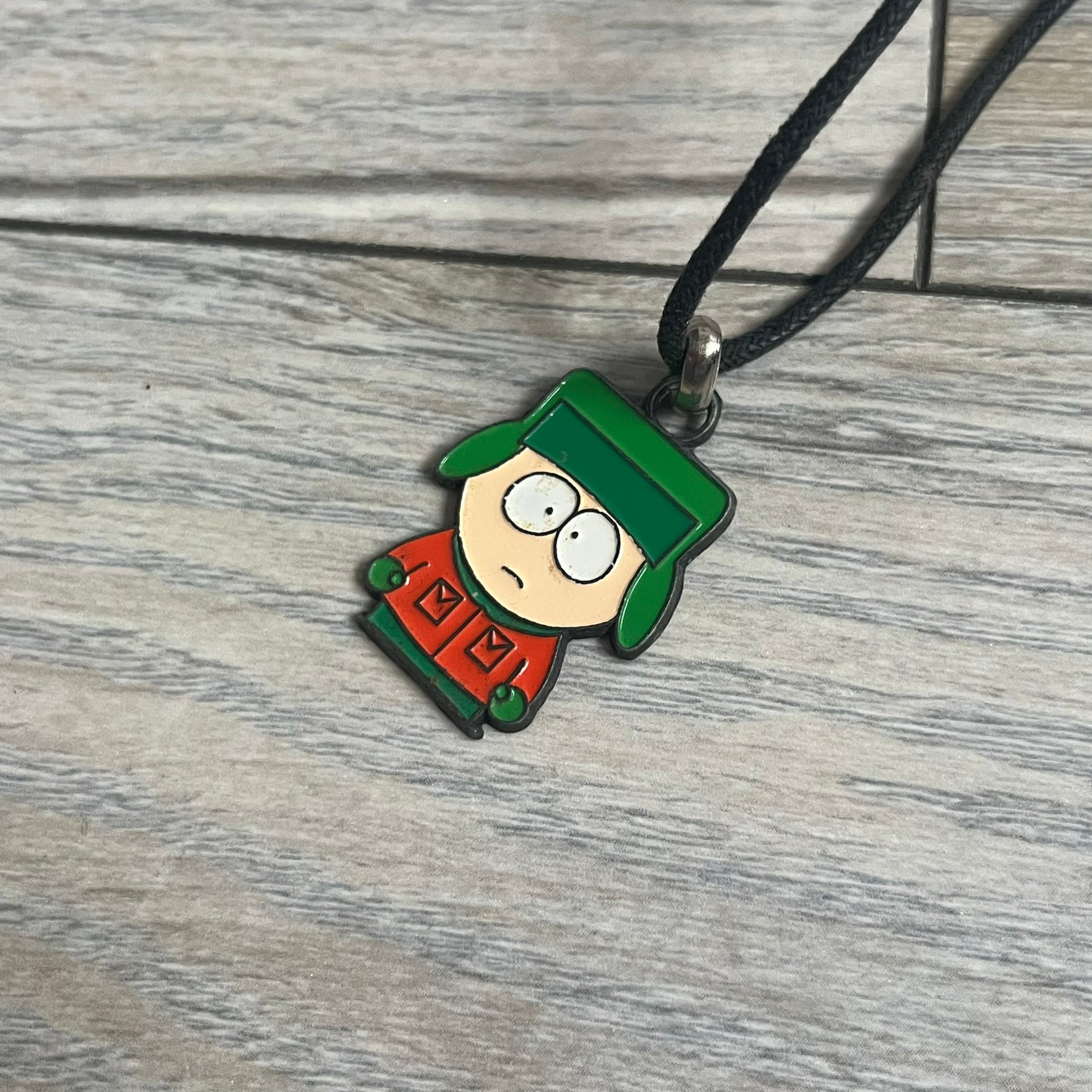South Park 2000 Kyle Necklace features a black cord necklace with a metal pendant shaped as Kyle from South Park. The back of the pendant is marked with 2000 Comedy Central and Sedesma licensing details.