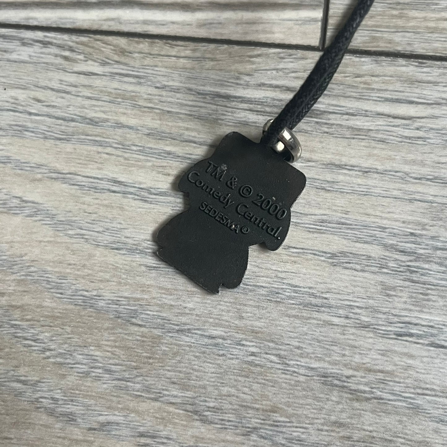 South Park 2000 Kyle Necklace features a black cord necklace with a metal pendant shaped as Kyle from South Park. The back of the pendant is marked with 2000 Comedy Central and Sedesma licensing details.