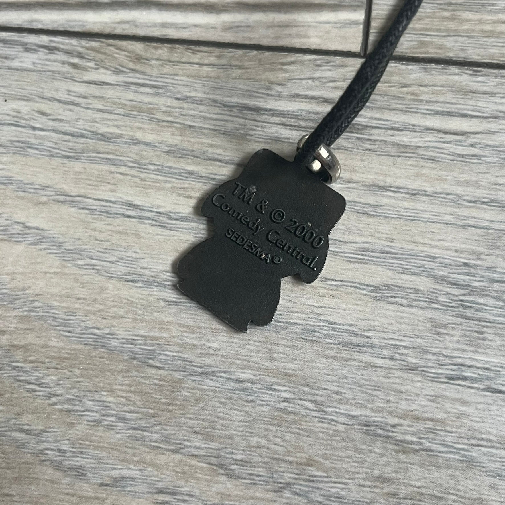 South Park 2000 Kyle Necklace features a black cord necklace with a metal pendant shaped as Kyle from South Park. The back of the pendant is marked with 2000 Comedy Central and Sedesma licensing details.