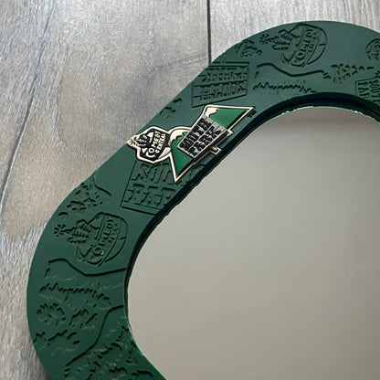 Small tabletop mirror with a molded rubber frame featuring all-over cutout logos for South Park and Comedy Central, along with leaf and tree motifs. The top is finished with a raised 3D South Park logo, while the bottom features 3D rubber figures of Cartman, Kenny, Kyle, and Stan standing at their bus stop. Marked with a 2000 Comedy Central copyright at the bottom, with a black backing and integrated stand.