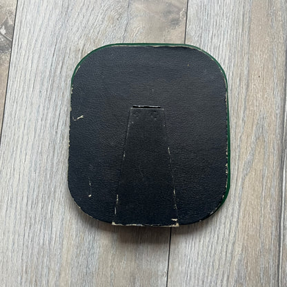 Small tabletop mirror with a molded rubber frame featuring all-over cutout logos for South Park and Comedy Central, along with leaf and tree motifs. The top is finished with a raised 3D South Park logo, while the bottom features 3D rubber figures of Cartman, Kenny, Kyle, and Stan standing at their bus stop. Marked with a 2000 Comedy Central copyright at the bottom, with a black backing and integrated stand.