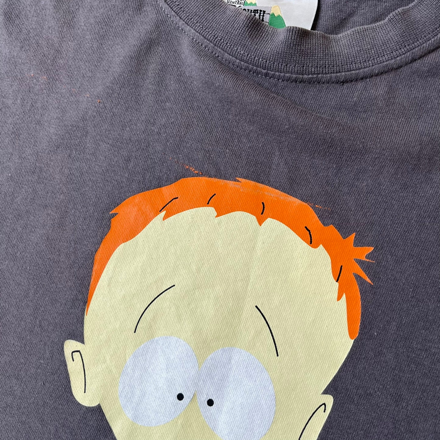South Park 2008 Timmy “I’m Special” Tee features a grey T-shirt with a front graphic of Timmy’s face above a blue bar with white “I’m Special” text. Small 2008 licensing and Comedy Central details are printed underneath. The back features a blue and white wheelchair-accessibility sign graphic. Includes a licensed South Park neck tag.
