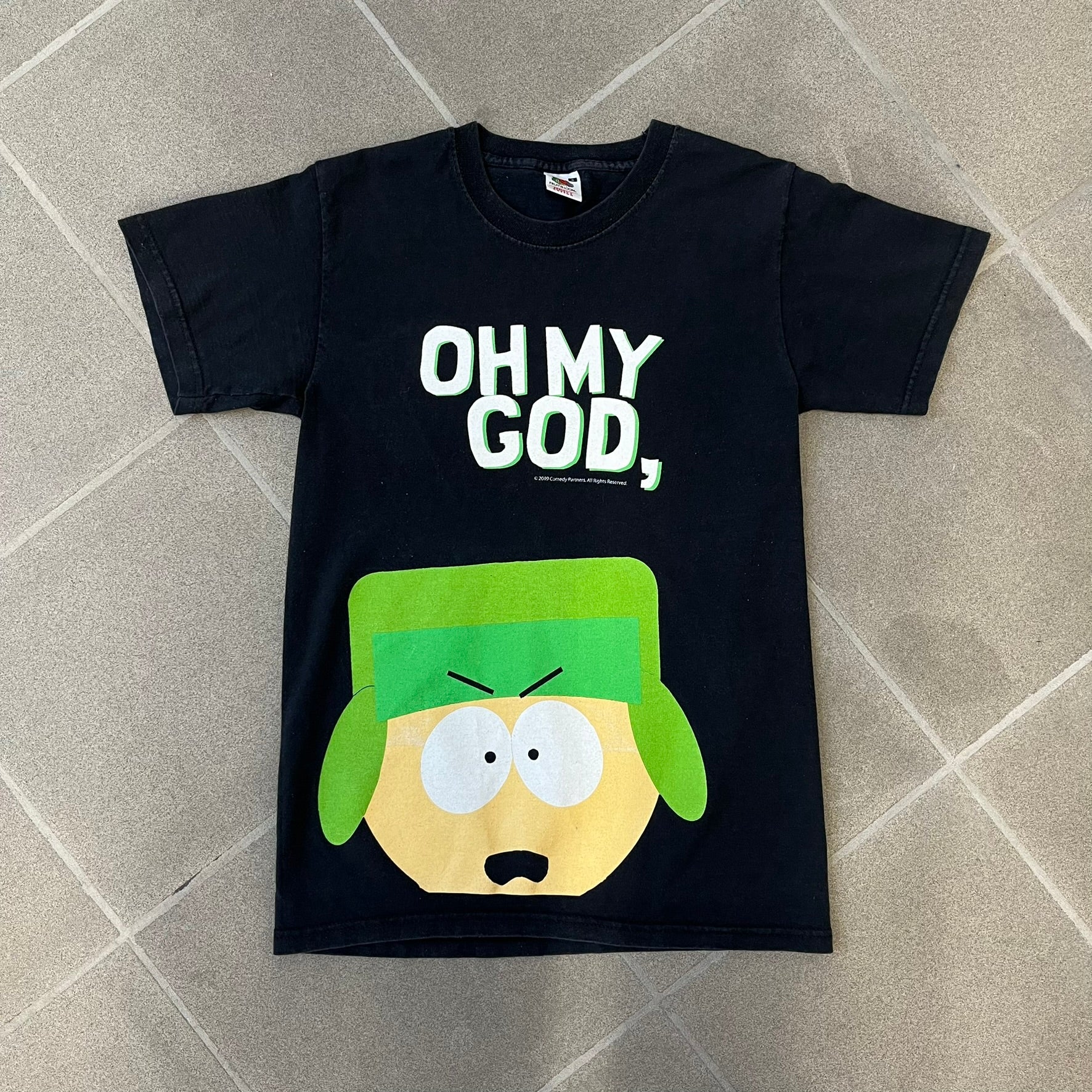 South Park 2009 “Oh My God, They Killed Kenny!” Tee is a black T-shirt made on a Fruit of the Loom blank. The front features a large graphic of Kyle with “Oh My God,” printed above and 2009 South Park licensing below. The back shows a stitched version of Kenny with “They Killed Kenny!” printed above the graphic.
