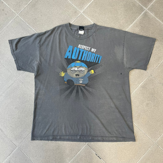 South Park 2009 “Respect My Authority” Gray Tee features a grey T-shirt with a front graphic of Cartman wearing a police uniform and running across a dotted cartoon-style background. Above the graphic is white and blue “Respect My Authority” text. The shirt has a South Park 2009 licensed neck tag and a heavily worn, distressed condition.
