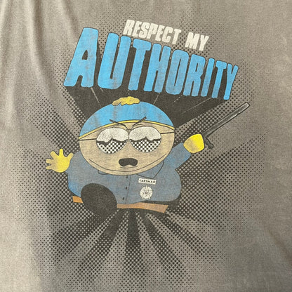 South Park 2009 “Respect My Authority” Gray Tee features a grey T-shirt with a front graphic of Cartman wearing a police uniform and running across a dotted cartoon-style background. Above the graphic is white and blue “Respect My Authority” text. The shirt has a South Park 2009 licensed neck tag and a heavily worn, distressed condition.
