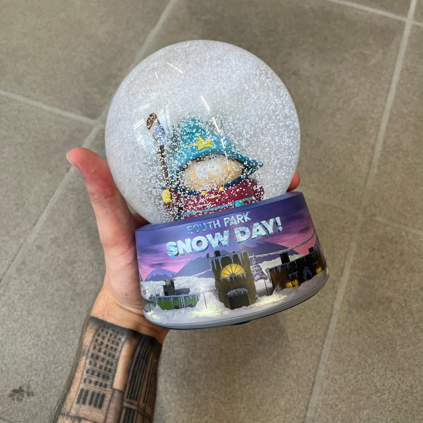 Exclusive South Park Snow Day Grand Wizard Cartman Snowglobe. Showcases Cartman in full wizard attire within a globe packed with dense snow for a humorous effect, making Cartman almost disappear beneath the flakes. Officially licensed piece with 2024 Comedy Partners text on the base.