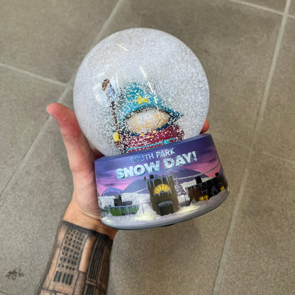 Exclusive South Park Snow Day Grand Wizard Cartman Snowglobe. Showcases Cartman in full wizard attire within a globe packed with dense snow for a humorous effect, making Cartman almost disappear beneath the flakes. Officially licensed piece with 2024 Comedy Partners text on the base.