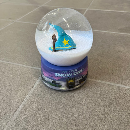 Exclusive South Park Snow Day Grand Wizard Cartman Snowglobe. Showcases Cartman in full wizard attire within a globe packed with dense snow for a humorous effect, making Cartman almost disappear beneath the flakes. Officially licensed piece with 2024 Comedy Partners text on the base.