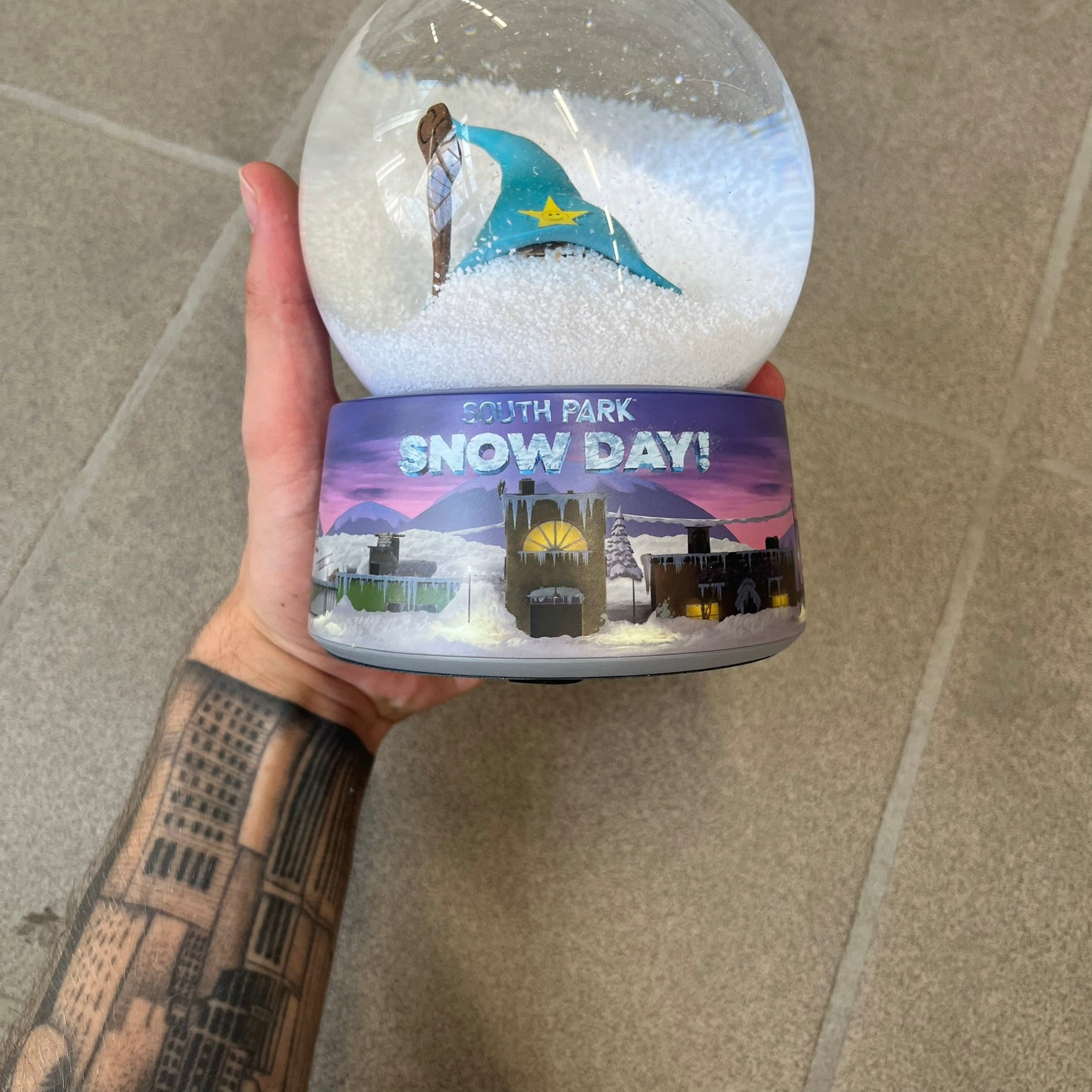 Exclusive South Park Snow Day Grand Wizard Cartman Snowglobe. Showcases Cartman in full wizard attire within a globe packed with dense snow for a humorous effect, making Cartman almost disappear beneath the flakes. Officially licensed piece with 2024 Comedy Partners text on the base.