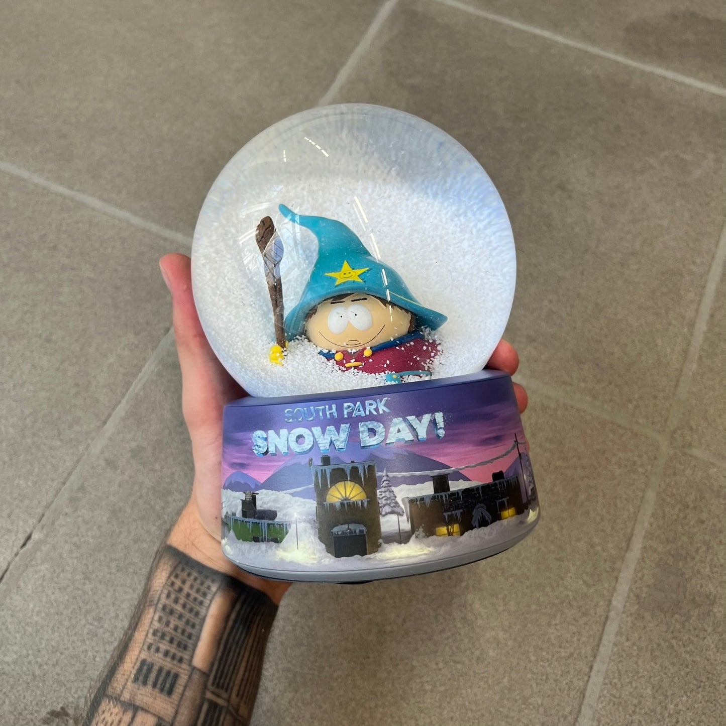 Exclusive South Park Snow Day Grand Wizard Cartman Snowglobe. Showcases Cartman in full wizard attire within a globe packed with dense snow for a humorous effect, making Cartman almost disappear beneath the flakes. Officially licensed piece with 2024 Comedy Partners text on the base.