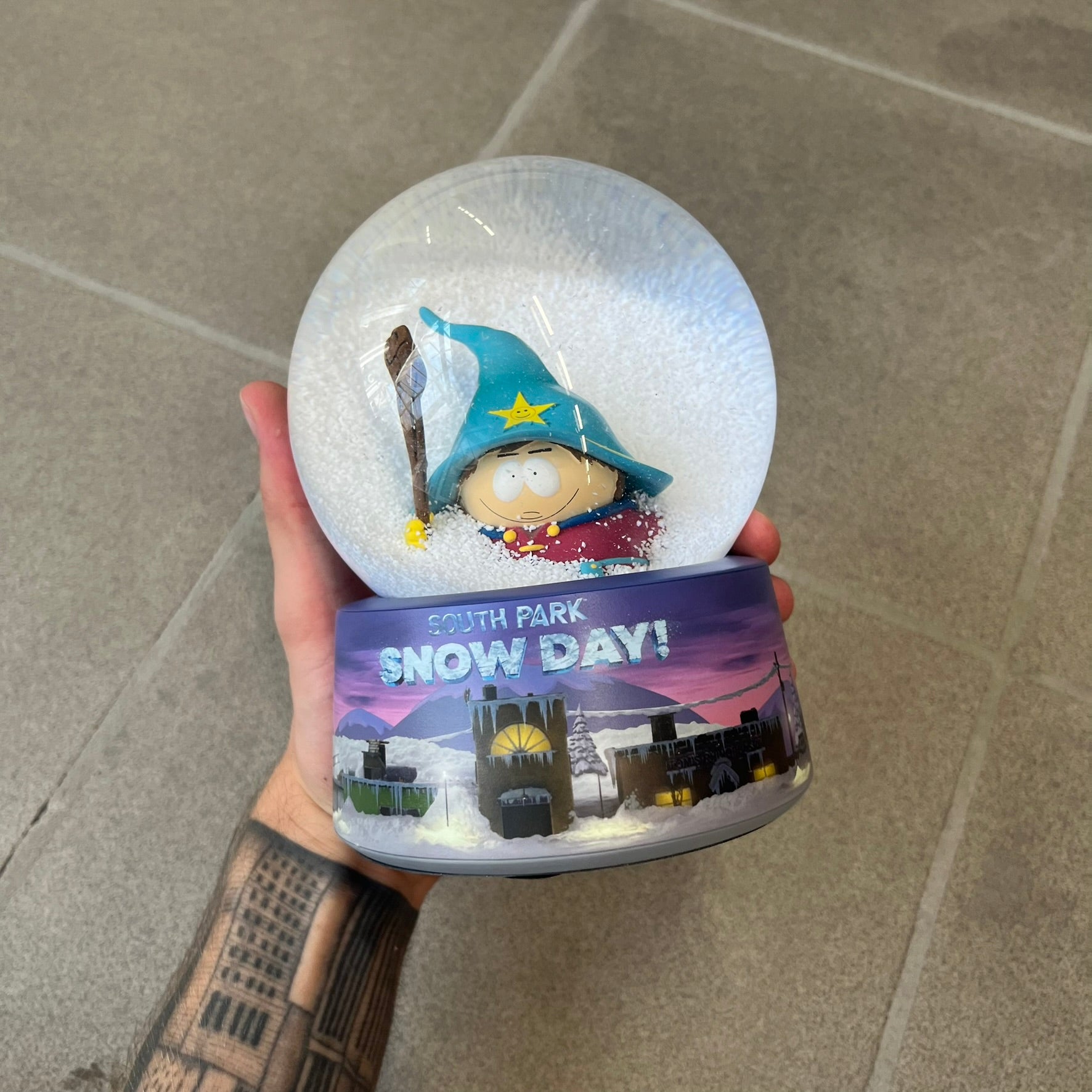 Exclusive South Park Snow Day Grand Wizard Cartman Snowglobe. Showcases Cartman in full wizard attire within a globe packed with dense snow for a humorous effect, making Cartman almost disappear beneath the flakes. Officially licensed piece with 2024 Comedy Partners text on the base.