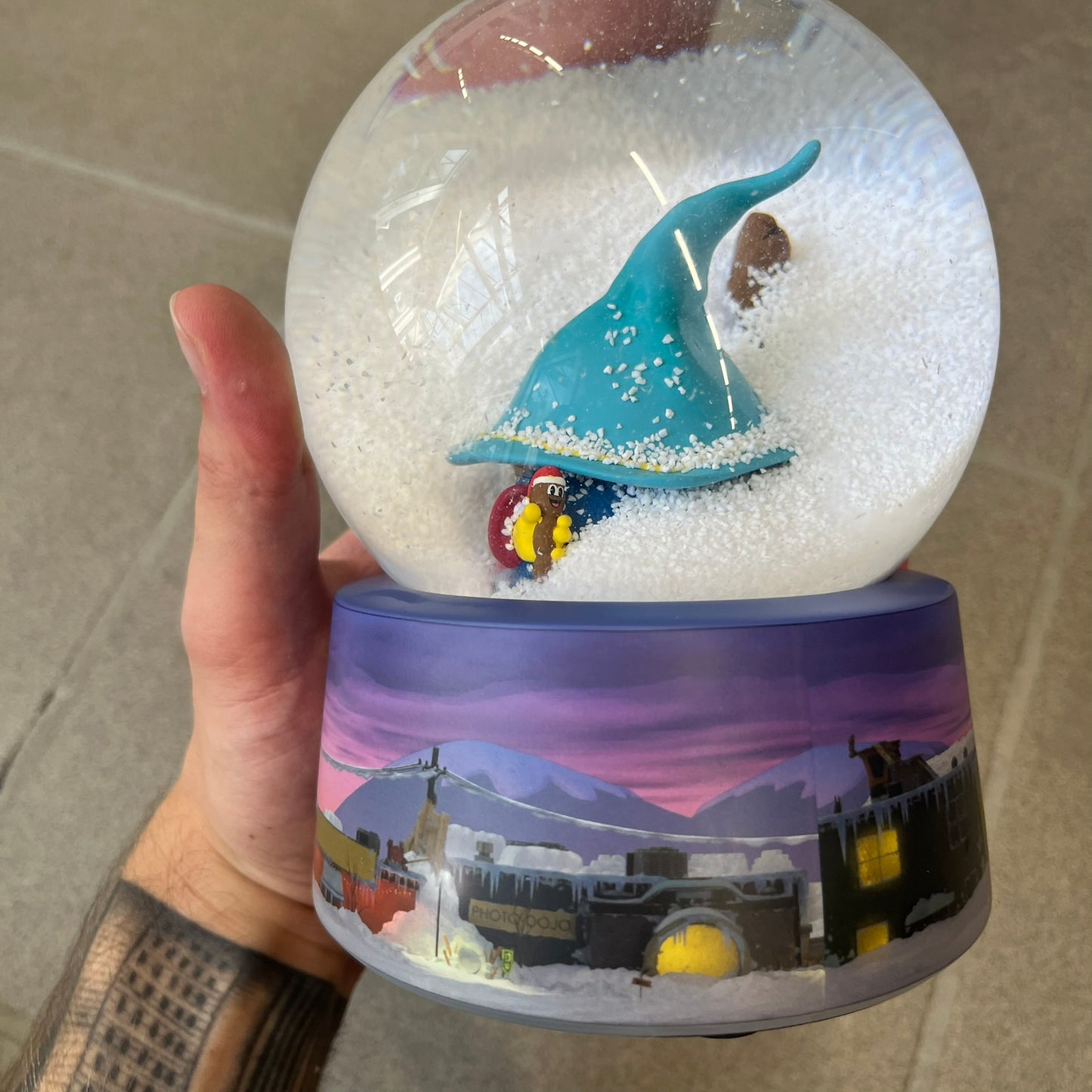 Exclusive South Park Snow Day Grand Wizard Cartman Snowglobe. Showcases Cartman in full wizard attire within a globe packed with dense snow for a humorous effect, making Cartman almost disappear beneath the flakes. Officially licensed piece with 2024 Comedy Partners text on the base.