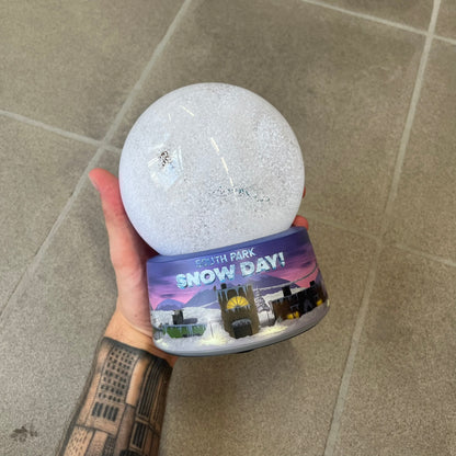 Exclusive South Park Snow Day Grand Wizard Cartman Snowglobe. Showcases Cartman in full wizard attire within a globe packed with dense snow for a humorous effect, making Cartman almost disappear beneath the flakes. Officially licensed piece with 2024 Comedy Partners text on the base.