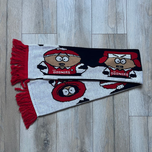 Vintage football scarf in white and black with red fringe / tassels, featuring South Park characters including Kenny, Cartman, and Kyle dressed in Arsenal kits with “Gooners” text. The character graphics appear on both sides of the scarf, with consistent coloring in white and red. Soft knit construction with a classic football scarf shape and finish.