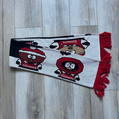 Vintage football scarf in white and black with red fringe / tassels, featuring South Park characters including Kenny, Cartman, and Kyle dressed in Arsenal kits with “Gooners” text. The character graphics appear on both sides of the scarf, with consistent coloring in white and red. Soft knit construction with a classic football scarf shape and finish.