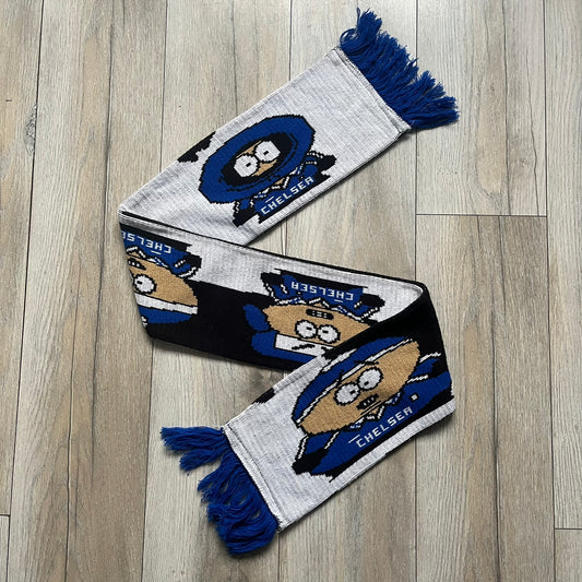Vintage football scarf in white and black with blue fringe / tassels, featuring South Park characters including Kenny, Cartman, and Kyle dressed in Chelsea kits. The character graphics appear on both sides of the scarf, with consistent coloring in blue. Soft knit construction with a classic football scarf shape and finish.