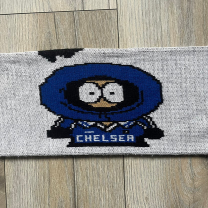 Vintage football scarf in white and black with blue fringe / tassels, featuring South Park characters including Kenny, Cartman, and Kyle dressed in Chelsea kits. The character graphics appear on both sides of the scarf, with consistent coloring in blue. Soft knit construction with a classic football scarf shape and finish.