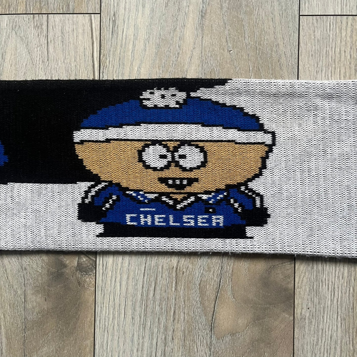 Vintage football scarf in white and black with blue fringe / tassels, featuring South Park characters including Kenny, Cartman, and Kyle dressed in Chelsea kits. The character graphics appear on both sides of the scarf, with consistent coloring in blue. Soft knit construction with a classic football scarf shape and finish.