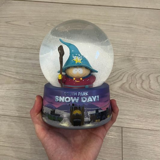 Exclusive South Park Snow Day Grand Wizard Cartman Snowglobe. Showcases Cartman in full wizard attire within a globe packed with dense snow for a humorous effect, making Cartman almost disappear beneath the flakes. Officially licensed piece with 2024 Comedy Partners text on the base.